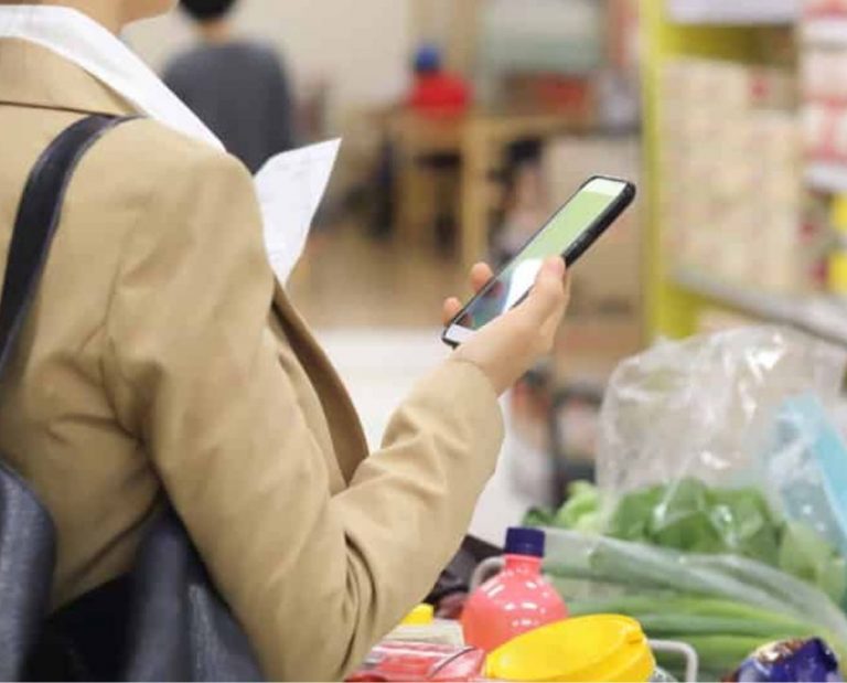 Mulher segura celular no supermercado com carrinho de compras