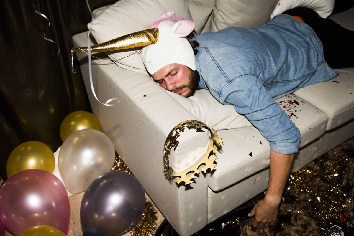 Homem vestido de unicórnio deitado no sofá com enfeites de festa ao redor